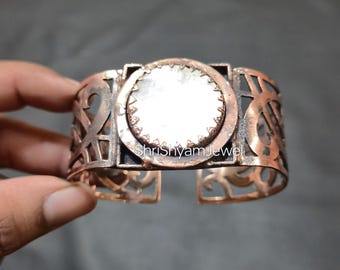 Può includere: Bracciale a polsino color rame con un design traforato. Il centro presenta una pietra circolare di colore chiaro incastonata in una cornice quadrata. Il bracciale ha il testo "ShriShyamJewel".