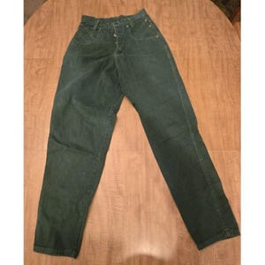 May include: Dark green denim jeans with a high waist and button fly. The jeans have a classic five-pocket design and are made of a durable denim fabric. The jeans are laid flat on a wooden surface.