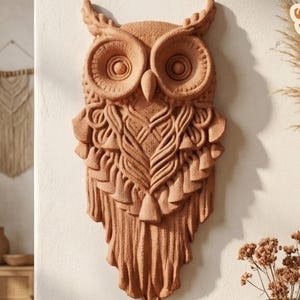 Op de afbeelding: Een terracotta-kleurige uil wanddecoratie met ingewikkelde gesneden details, waaronder veren en gezichtskenmerken. De uil wordt weergegeven op een lichte muur, met daaronder een houten plank met potplanten en vazen. De afbeelding bevat de tekst "Only Digital Files 3D STL Download" en "*Test Print".