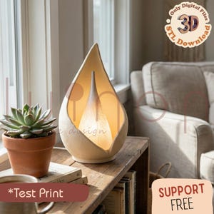 May include: A cream-coloured, teardrop-shaped lamp with a warm, glowing interior. The lamp sits on a wooden table next to a potted succulent. The image also includes the text "*Test Print" and "SUPPORT FREE".
