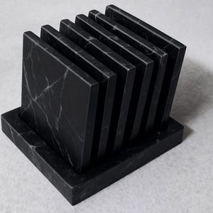 Puede incluir: Un juego de seis posavasos cuadrados de m&aacute;rmol negro con vetas blancas, exhibidos en un soporte rectangular a juego. Los posavasos est&aacute;n dispuestos en forma de abanico, mostrando sus superficies pulidas. Una adici&oacute;n elegante a cualquier hogar.