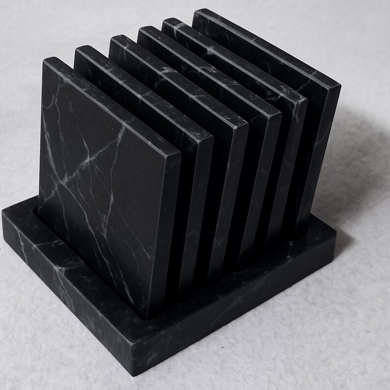 Puede incluir: Un juego de seis posavasos cuadrados de m&aacute;rmol negro con vetas blancas, exhibidos en un soporte rectangular a juego. Los posavasos est&aacute;n dispuestos en forma de abanico, mostrando sus superficies pulidas. Una adici&oacute;n elegante a cualquier hogar.