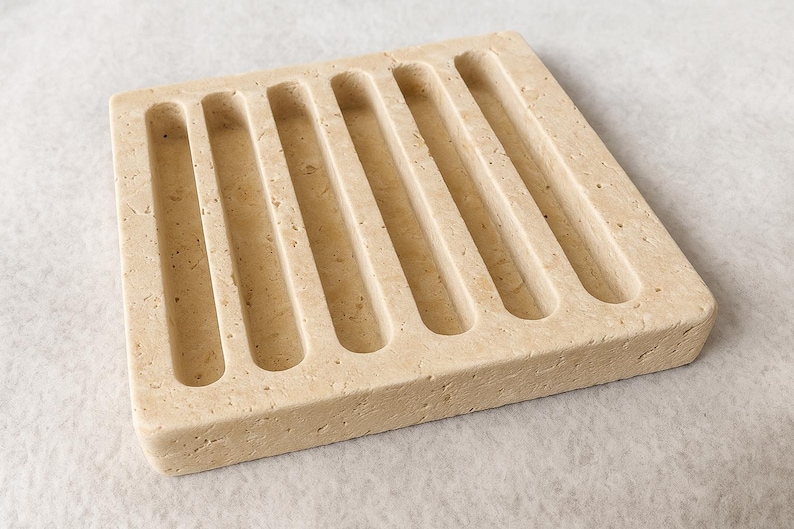 Puede incluir: Un jabonera cuadrada beige con seis ranuras paralelas y curvas. La jabonera est&aacute; hecha de un material de piedra texturizada y est&aacute; dise&ntilde;ada para sostener una pastilla de jab&oacute;n. El color neutro y el dise&ntilde;o sencillo la hacen adecuada para cualquier ba&ntilde;o.