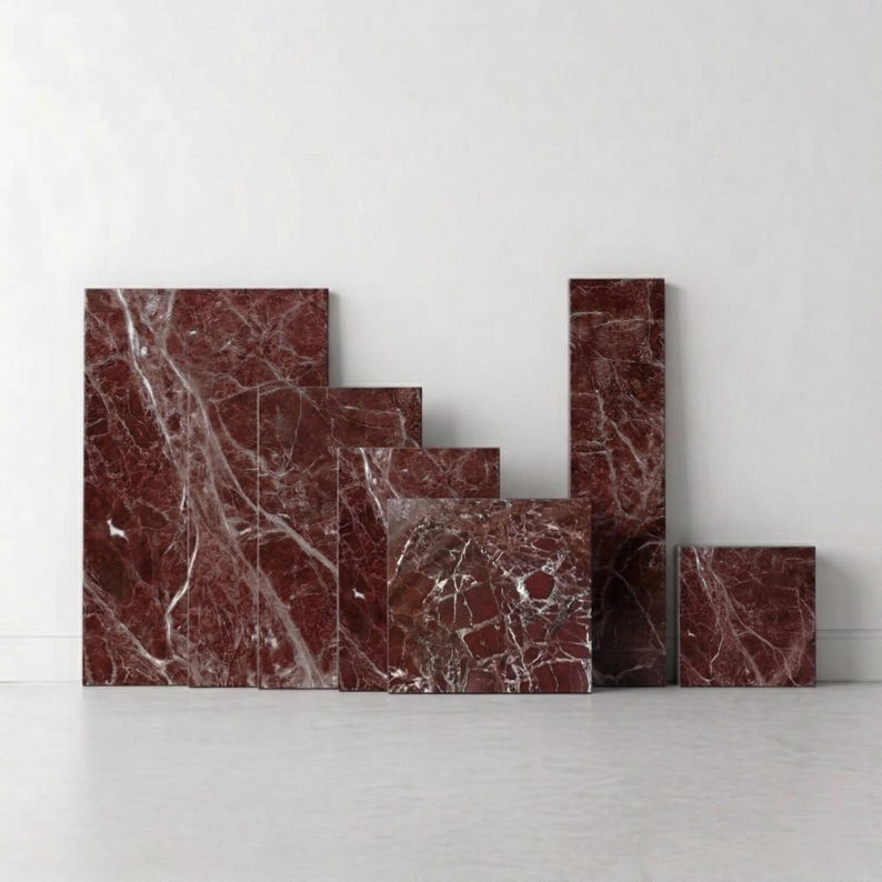 May include: A collection of red marble tiles in various rectangular and square shapes. The tiles have white veining throughout, creating a natural pattern. The tiles are arranged against a white wall and floor.