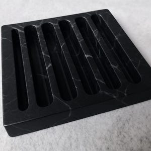 Puede incluir: Una bandeja cuadrada de m&aacute;rmol negro con seis ranuras largas y paralelas. La bandeja tiene un acabado pulido y un sutil veteado blanco en toda la piedra oscura. Las ranuras est&aacute;n espaciadas uniformemente y tienen extremos redondeados.