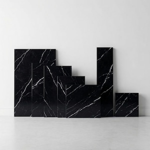 Puede incluir: Conjunto de losas de mármol negro con vetas blancas, dispuestas en diversos tamaños y formas. Las losas son rectangulares y cuadradas, creando una exhibición moderna y minimalista. Las superficies pulidas reflejan la luz, resaltando los patrones naturales.