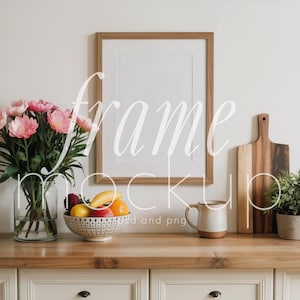 May include: A wooden framed mockup with a white mat, set on a light wood surface. A glass vase with pink flowers, a bowl of fruit, a mug, a cutting board, and a potted plant are arranged on the surface. The text "frame mockup" is overlaid on the image.