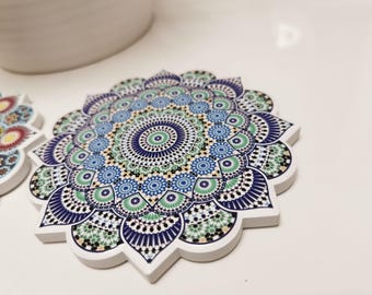 May include: A decorative coaster with a detailed mandala design. The coaster features a white border and a colorful pattern of blue, green, and white geometric shapes. The design is symmetrical and intricate, creating a visually appealing accent piece.