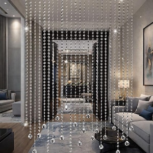 May include: A beaded curtain made of clear, sparkling crystal beads hangs in a doorway. The beads are strung in vertical strands, creating a shimmering effect. The curtain adds a touch of elegance and glamour to the interior space.