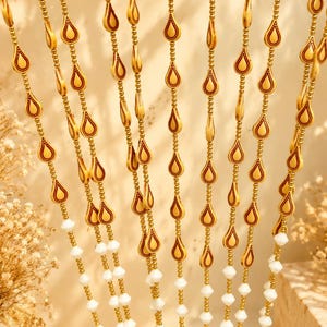 May include: A decorative beaded curtain featuring multiple vertical strands. Each strand consists of alternating white faceted beads and gold-toned teardrop-shaped pendants with dark brown centers, creating a repeating pattern of hanging elements.