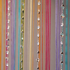 Puede incluir: Cortina de cuentas coloridas con hilos de varios colores, incluyendo rosa, morado y turquesa. Algunos hilos presentan acentos de cristal en forma de diamante, creando un diseño decorativo y llamativo.