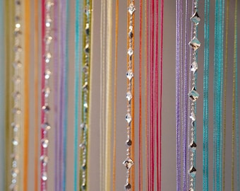 May include: Colorful beaded curtain with strands of various colors, including pink, purple, and turquoise. Some strands feature diamond-shaped crystal accents, creating a decorative and eye-catching design.