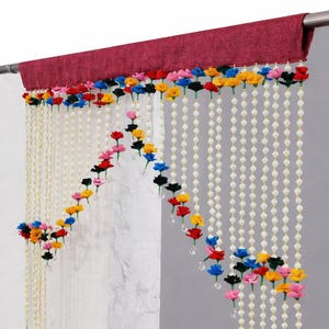 May include: A decorative curtain with a burgundy header and strings of white beads. Colorful fabric flowers in red, pink, yellow, blue, and black are attached to the strings, creating a floral design. Clear crystal accents hang from the strings.
