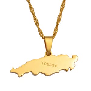 May include: A gold-colored necklace with a pendant shaped like the island of Tobago. The pendant has the word "TOBAGO" engraved on it. The chain is a twisted rope design.
