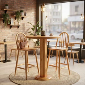 May include: A cafe interior with light wood furniture. Two high-backed chairs and a round table are in the foreground. A small handbag rests on one chair. The table has a cylindrical base. Other tables and chairs are visible.