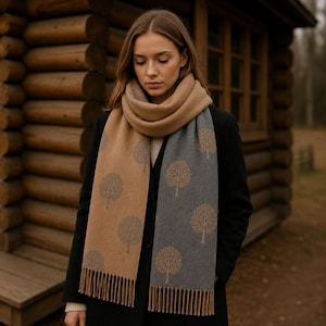 Puede incluir: Una bufanda reversible con diseño bicolor, un lado beige con motivos de árboles grises y un lado gris con motivos de árboles beige. La bufanda tiene una textura suave y está rematada con flecos largos y rectos en ambos extremos.
