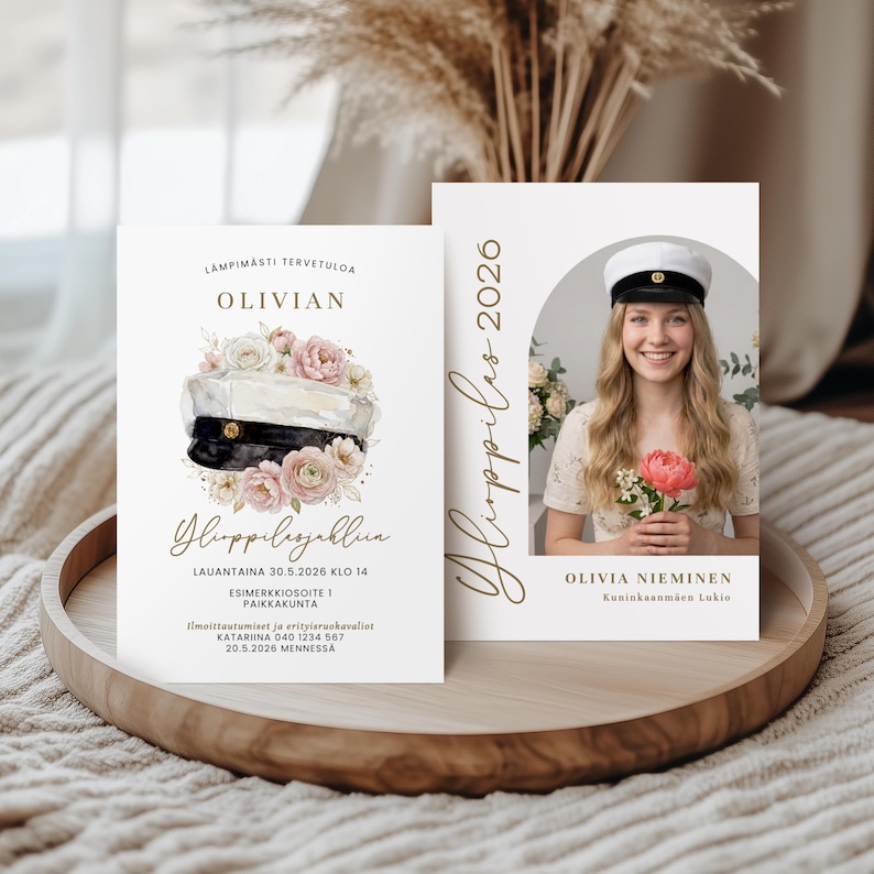 May include: Two graduation announcement cards on a wooden tray. The left card features text and a watercolor illustration of a graduation cap and flowers. The right card has a photo of a smiling woman holding flowers, with text and the year 2026.