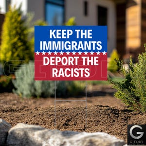 May include: A yard sign with the text "KEEP THE IMMIGRANTS, DEPORT THE RACISTS" in white letters on a blue and red background. The sign is displayed outdoors, planted in the ground with a metal stake.