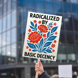 Puede incluir: Una persona sostiene un cartel rectangular con el texto "RADICALIZED BY BASIC DECENCY". El cartel tiene un dise&ntilde;o floral en rojo y azul. El fondo es una vista borrosa de un edificio moderno.