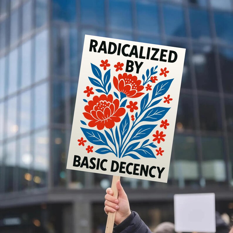 Puede incluir: Una persona sostiene un cartel rectangular con el texto "RADICALIZED BY BASIC DECENCY". El cartel tiene un dise&ntilde;o floral en rojo y azul. El fondo es una vista borrosa de un edificio moderno.