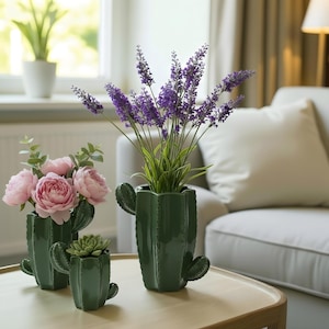 Può includere: Tre vasi verdi in ceramica a forma di cactus di diverse dimensioni, ciascuno con piante. Il vaso più grande contiene lavanda viola, quello medio peonie rosa e il più piccolo una succulenta. I vasi sono su un tavolo marrone chiaro.