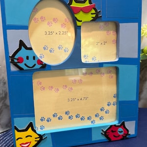 May include: A blue wooden picture frame with three openings of varying sizes. The frame has cat-themed decorations and paw print accents. The openings measure 3.25" x 2.25", 2" x 2", and 3.25" x 4.75".