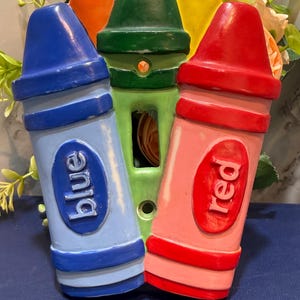 Könnte beinhalten: Ein skurriles, stiftförmiges Dekor in Blau, Grün und Rot. Der blaue Stift ist mit "blue" beschriftet, und der rote Stift ist mit "red" beschriftet. Die Stifte sind vor einem floralen Hintergrund angeordnet.