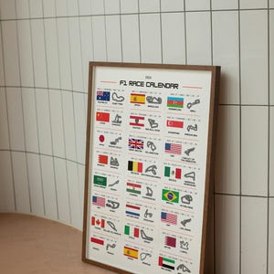 Puede incluir: Un calendario de carreras de F1 de 2026 enmarcado. El calendario presenta un fondo blanco con texto negro y contornos de circuitos. Las banderas de diferentes países se muestran encima de cada lugar de la carrera. El marco es de madera marrón.