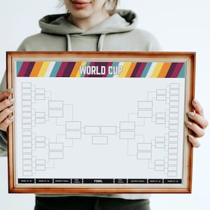 May include: A wooden framed World Cup bracket chart. The chart features a bracket layout with boxes for teams and the text "WORLD CUP" at the top. The top of the chart has a colourful striped design.