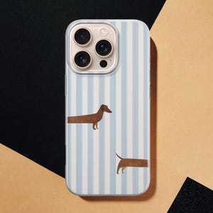 May include: A smartphone case with a light blue and white striped design. The case features two brown dachshund illustrations. The phone case is shown on a black and tan background.