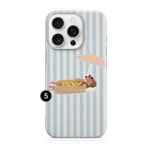May include: A phone case with a light blue and white striped design. The case features a cartoon illustration of a hot dog wearing sunglasses and relaxing under a peach-coloured umbrella. The hot dog has yellow mustard.