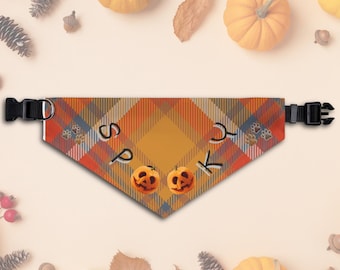Op de afbeelding: Een Halloween-thema bandana voor huisdieren met een oranje, gele en rode ruitpatroon. De bandana heeft het woord "Spook", twee uitgesneden pompoengezichten en pootafdrukken. Verstelbare zwarte gesp.