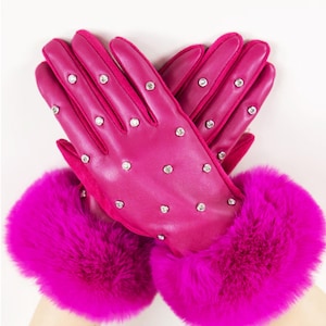 Könnte beinhalten: Ein Paar leuchtend pinkfarbene Handschuhe mit luxuriösem Design. Die Handschuhe sind mit kleinen, funkelnden Verzierungen versehen und verfügen über flauschige, passende Pelzbündchen. Die Handschuhe sind aus einem glatten Material gefertigt, perfekt für kaltes Wetter.