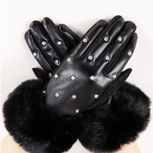 Könnte beinhalten: Schwarze Lederhandschuhe mit Kunstfellbündchen. Die Handschuhe sind mit kleinen, funkelnden Strasssteinen besetzt. Die Handschuhe werden vor einem weißen Hintergrund gezeigt.