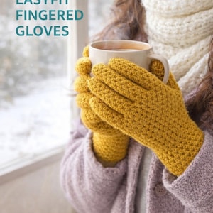 Op de afbeelding: Mosterdgele gehaakte handschoenen, onderdeel van een haakpatroon, worden rond een witte mok gehouden. De handschoenen hebben een gestructureerd steekpatroon. De tekst "Crochet Pattern EASYFIT FINGERED GLOVES" is zichtbaar. Een gezellig winterthema.