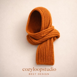 May include: An orange-brown knitted hood and scarf set. The hood is attached to the scarf, creating a seamless design. The text "cozyloopstudio BEST DESIGN" is printed at the bottom of the image. The knitwear is made of a thick, ribbed material.