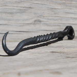 Könnte beinhalten: Ein schwarzer Haken aus Metall mit einem gedrehten Griff. Der Haken ist aus geschmiedetem Stahl und hat eine rustikale Oberfläche.