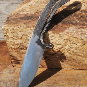 K&ouml;nnte beinhalten: Ein handgeschmiedetes Messer mit einem gedrehten Griff und einer scharfen Klinge. Das Messer liegt auf einem St&uuml;ck Holz.