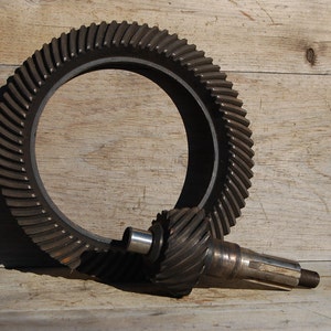 May include: A set of two metal gears, one large and ring-shaped, the other smaller and cylindrical. The gears are lying on a wooden surface.