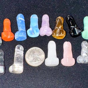 Könnte beinhalten: Eine Sammlung kleiner, phallusförmiger Skulpturen in verschiedenen Farben und Materialien, darunter Bergkristall, Marmor und polierter Stein. Ein US-Vierteldollar ist zum Größenvergleich enthalten.