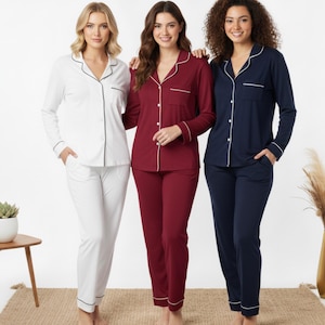 Puede incluir: Tres conjuntos de pijamas en blanco, burdeos y azul marino. Cada conjunto incluye una camisa abotonada de manga larga y pantalones a juego. Los pijamas tienen ribetes blancos en los bordes y están hechos de un material suave y cómodo.