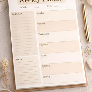 Op de afbeelding: Een weekplanner met de titel "Weekly Planner". De planner heeft secties voor elke dag van de week, een takenlijst en notities. Een gouden pen, paperclips en andere kantoorartikelen zijn rond de planner gerangschikt.