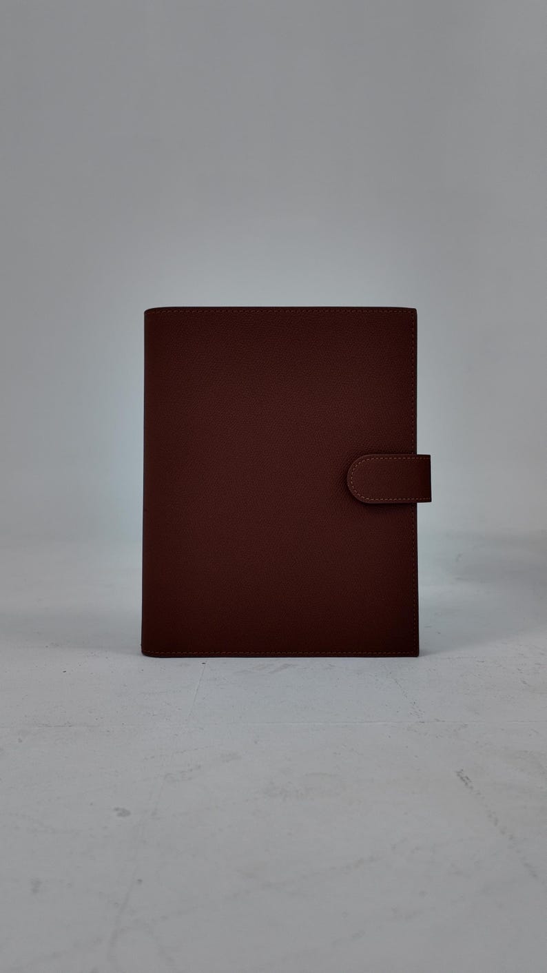 Peut inclure: Un journal en cuir marron au design simple. Le journal a une forme rectangulaire avec des coins arrondis et une fermeture &agrave; rabat. La couverture est d'une couleur marron riche et unie, et la fermeture est une languette en cuir marron assortie.