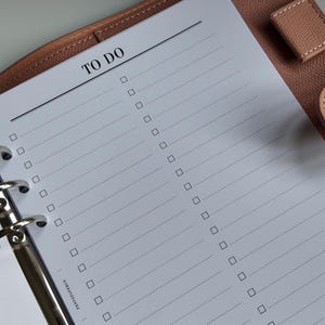 May include: A planner with a "TO DO" list printed on white paper. The paper is inside a brown leather binder with silver metal rings. The list has checkboxes and dotted lines for notes. The brand name "PENTOPAPERCO" is printed at the bottom.