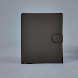 Peut inclure: Un journal en cuir gris avec une fermeture &agrave; bouton-pression. La couverture est de couleur grise unie et sourde avec une surface textur&eacute;e. Le journal est rectangulaire et semble ferm&eacute;, avec une fermeture &agrave; languette sur le c&ocirc;t&eacute; droit.