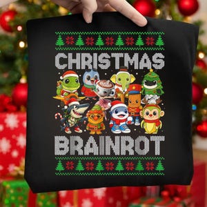 May include: Black tote bag with a festive Christmas design. The design features the text "CHRISTMAS BRAINROT" in white, surrounded by cartoon characters wearing Santa hats and other holiday attire. Green and red Christmas tree patterns are at the top and bottom.