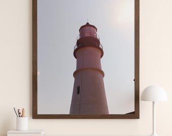 May include: A framed print of a lighthouse, featuring a white tower with a red top and a dark brown frame. The image is set against a pale sky, with a desk and chair in the foreground.