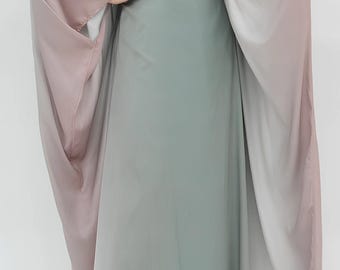May include: A flowing, floor-length dress in a soft, muted green. The dress features wide, draped sleeves that transition from a dusty rose to a pale white. The overall design is elegant and suitable for special occasions.