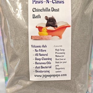 Może przedstawiać: Worek z kąpielą pyłową dla szynszyli z etykietą z napisem "Paws-N-Claws Chinchilla Dust Bath". Etykieta przedstawia szynszylę w wannie z gumową kaczką. Worek zawiera około 907 gramów popiołu wulkanicznego.