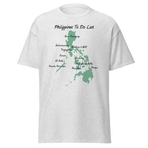 May include: Light gray t-shirt with the text "Philippines To Do List" above a green map of the Philippines. The map highlights various locations, including Rice Terraces, Boracay, and Chocolate Hills. A casual tee for travel enthusiasts.